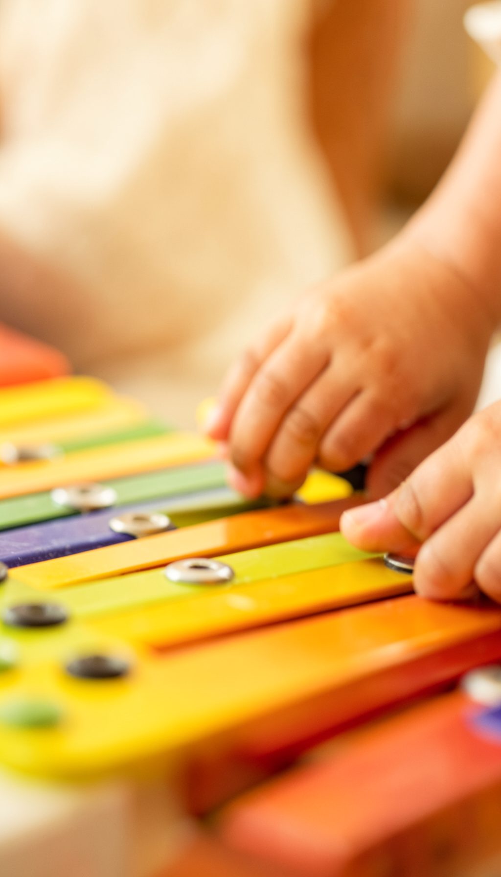 Close-up of a child's hands tapping a bright xylophone with a mallet, soft warm light and gentle amber tones in the background