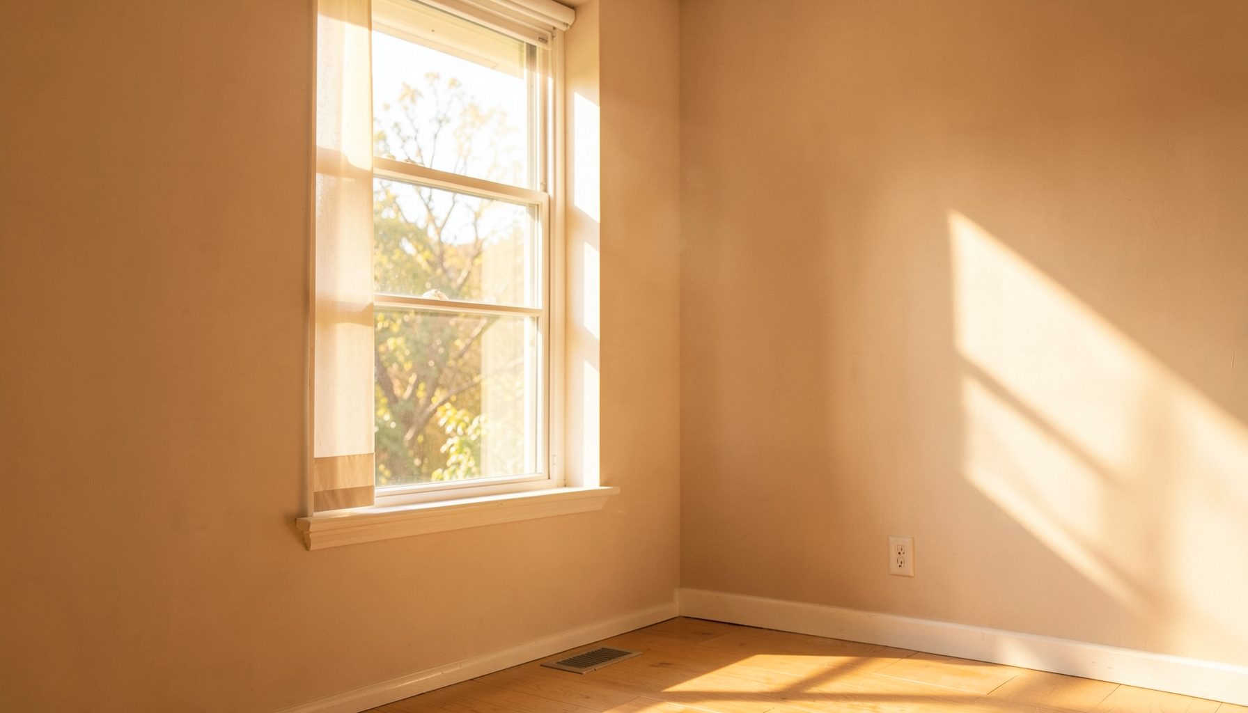 Warm sunlit room with soft beige walls and a large window, gentle golden light spilling across a calm, welcoming interior